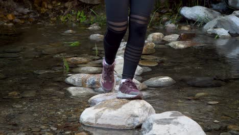 young woman skipping over boulders in creek close up