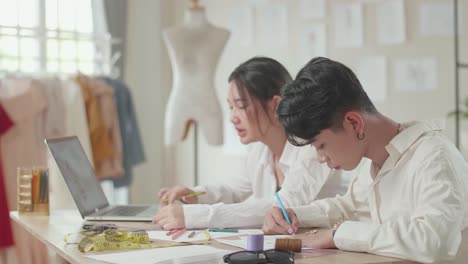 two fashion designers working with laptop and sketching at fashion design studio