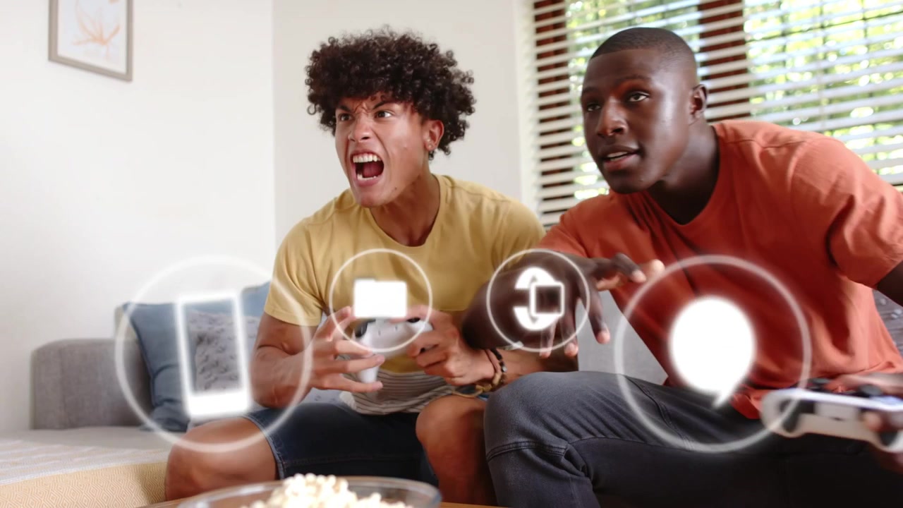 Two male players pressing controllers in living room, gaming as HUD icons floating across, smiling