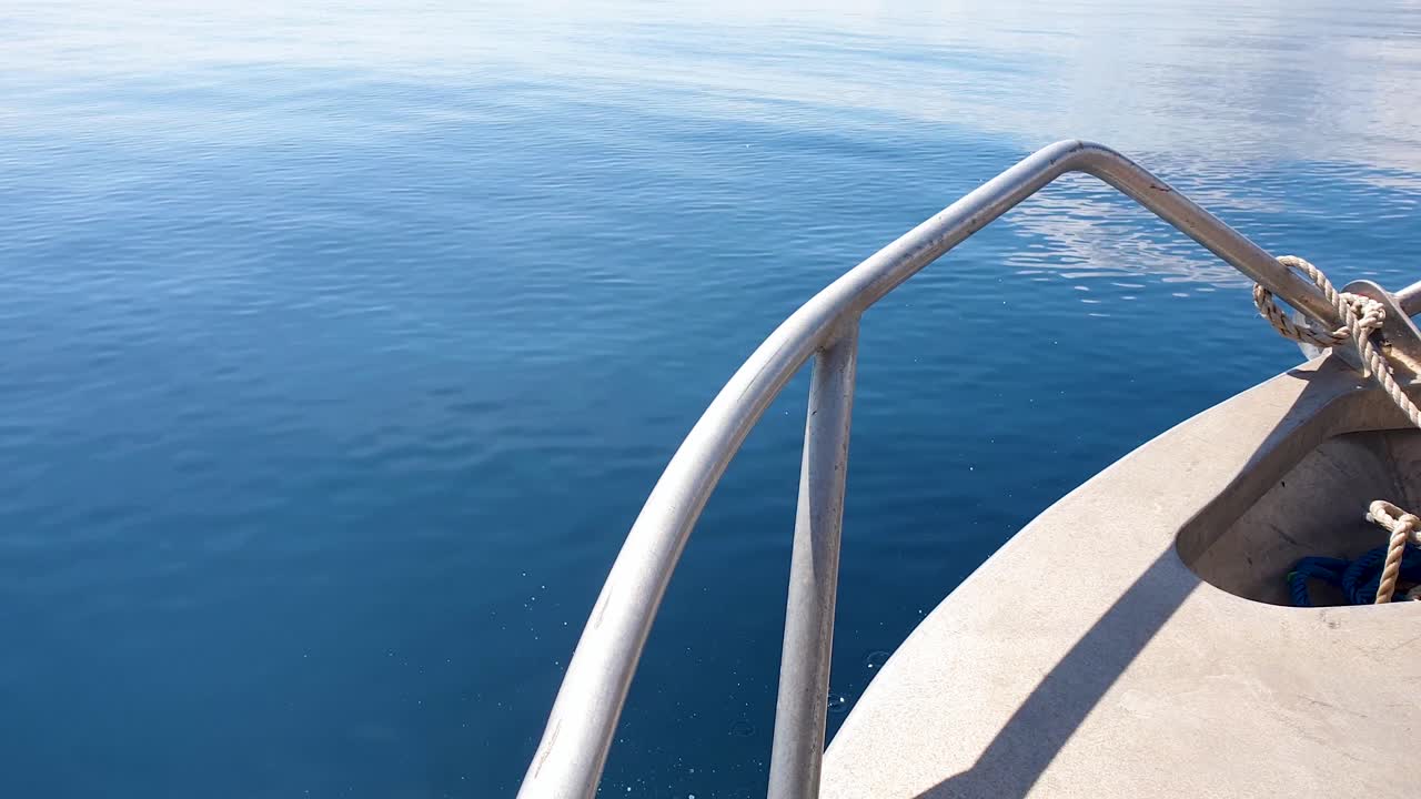 con vistas a la proa del barco de pesca de metal rozando y moviéndose sobre un hermoso día soleado con agua plana, tranquila y azul profundo del océano