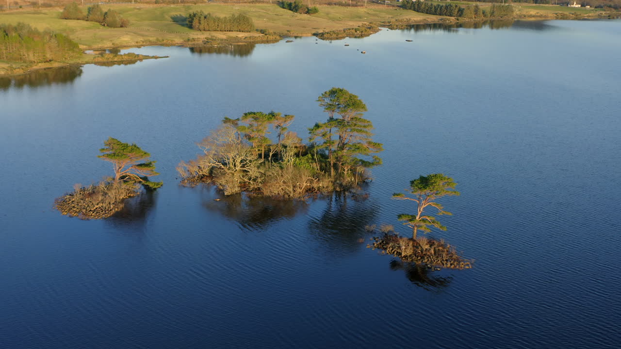 Aerial orbit pullback across Lough Bofin in Ireland, highlighting vibrant islands and crystal clear lake reflections at magic hour, Connemara, Galway, Ireland
