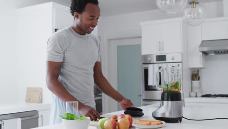 Man-Wearing-Pyjamas-Standing-In-Kitchen-Puts-Fresh--Fruit-And-Vegetables-Into-Blender-For-Smoothie