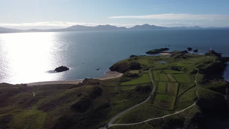 aerial view descending to ynys llanddwyn welsh island with shimmering ocean and misty snowdonia mountain range across the sunrise skyline