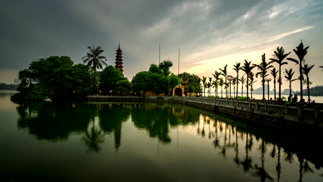 time lapse of tran quoc pagoda as visitors walk along bridge, serene lake reflections, hanoi, vietnam