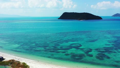 Beautiful-white-sandy-stripe-beach-washed-by-calm-clear-water-of-turquoise-lagoon-with-tropical-islands-background-and-bright-sky-with-clouds-in-Thailand