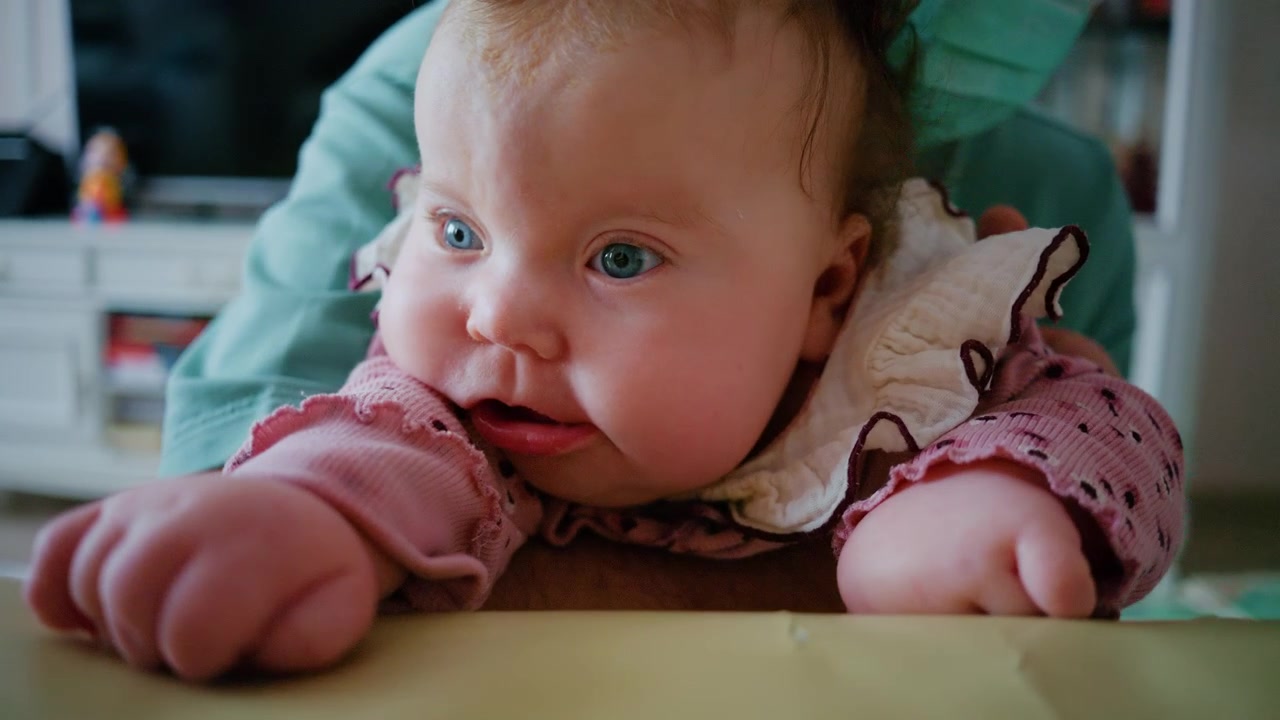 Nærbilde av en baby som holdes forsiktig oppreist på et polstret behandlingsbord under en pediatrisk terapisesjon.