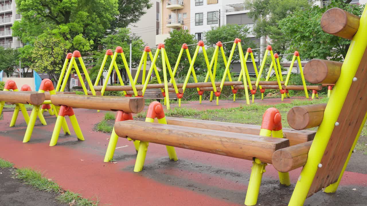 A low-angle, wide shot of a series of wooden balance beams that are part of a jungle gym in a park