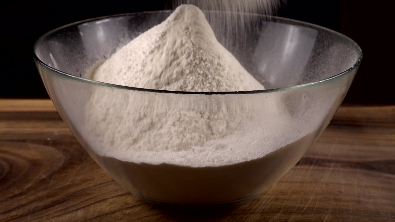 Mengayak tepung menggunakan saringan ke dalam mangkuk kaca di dapur.