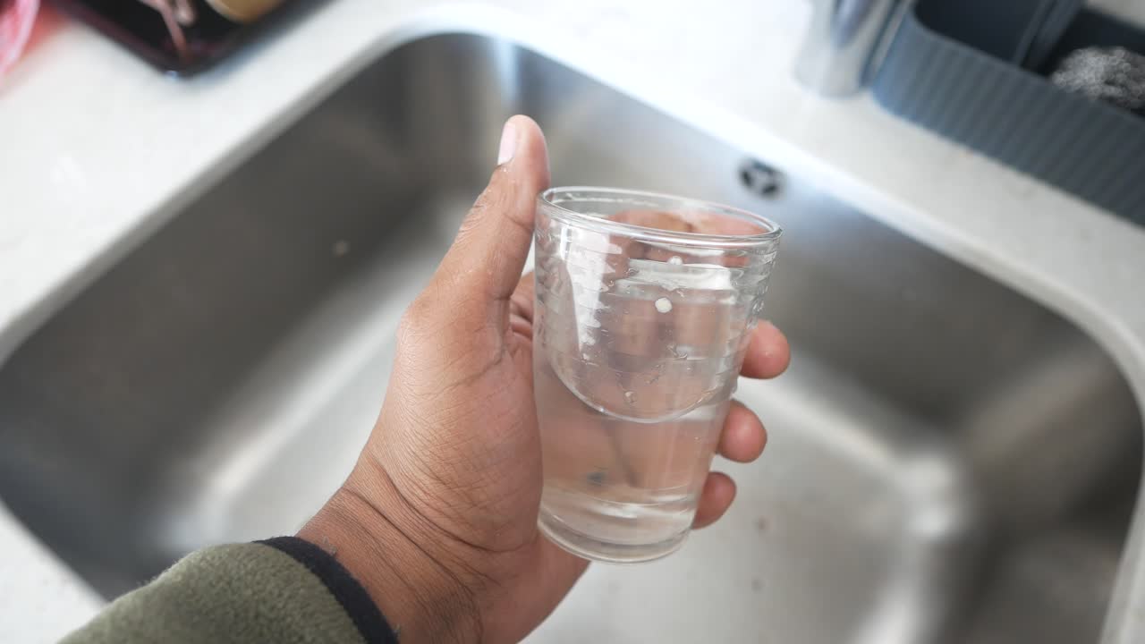 Hand holding a glass of water near a kitchen sink