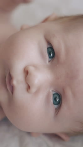 adorable infant boy with fair hair and large blue eyes lies on table and mother pets blond head extreme close view