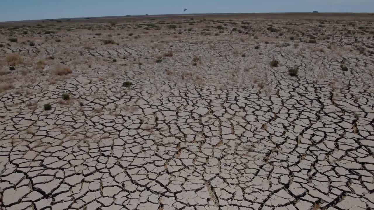 Aerial video captures a vast, cracked desert landscape under a clear sky, emphasizing the harsh