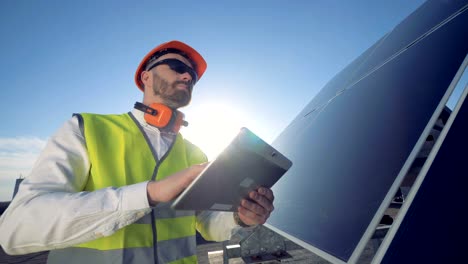 male engineer is standing on a rooftop near a solar battery with a tablet computer
