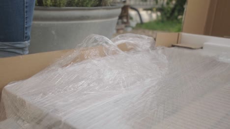 fotografía documental de bajo ángulo de una hembra abriendo un paquete con un cortador de cajas, cortando la lámina y quitándola, construyendo muebles para el exterior