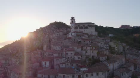 Aldea-De-Artena-En-La-Ladera-De-La-Montaña-Con-La-Luz-Del-Sol-De-La-Mañana-De-La-Iglesia-Alcanzando-Su-Punto-Máximo-Desde-El-Borde-De-La-Colina,-Antena