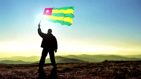 successful silhouette man winner waving togo flag on top of the mountain peak, cinemagraph loop background