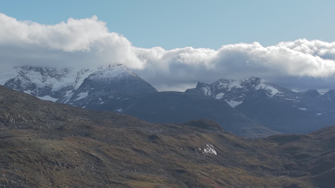 Backwards flying drone footage showing clouds over mountains and autumn colored hills in Jotunheimen National Park
