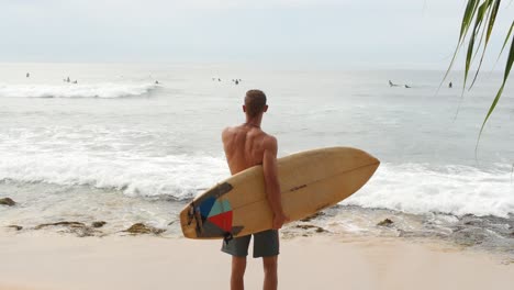 man walking towards waves with surfboard on tropical beach in sri lanka