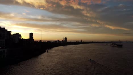Aerial-drone-shot-of-Puerto-Norte-Atardecer,-Argentina-along-the-coastline-of-the-parana-river-with-ship-and-motor-boats-passing-by-in-the-evening-time