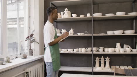 young american male clerk writing on a clipboard and making an inventory of ceramics in the pottery shop