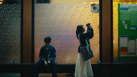 man sitting on bus stop station listening music being approach by a creative woman filmmaker with camera
