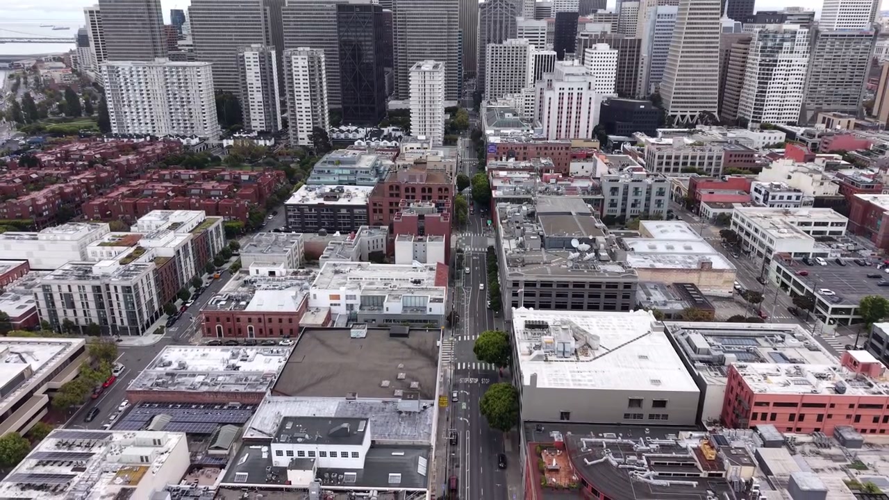 Dynamic aerial footage showcasing a dramatic drone pull out over a major street lined with modern high-rises, diverse urban buildings, and striking downtown architecture under diffuse daylight.