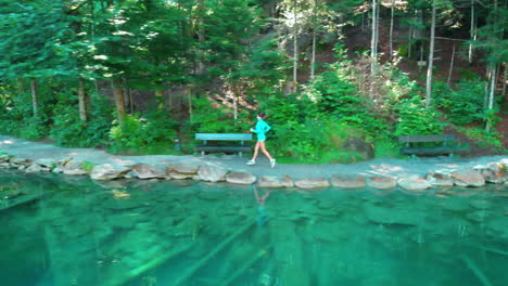 wide drone shot from side of older sporty woman running by a beautiful lake in nature with lens flares