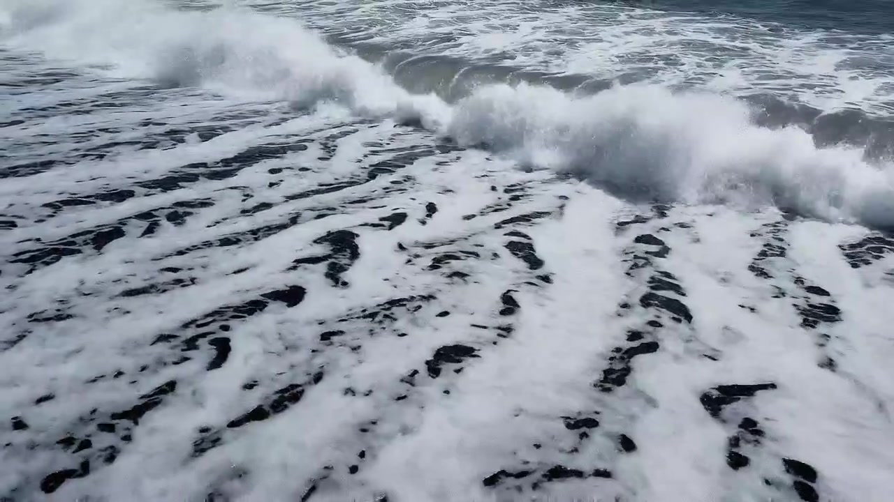 White sea foam washing over a black sand beach