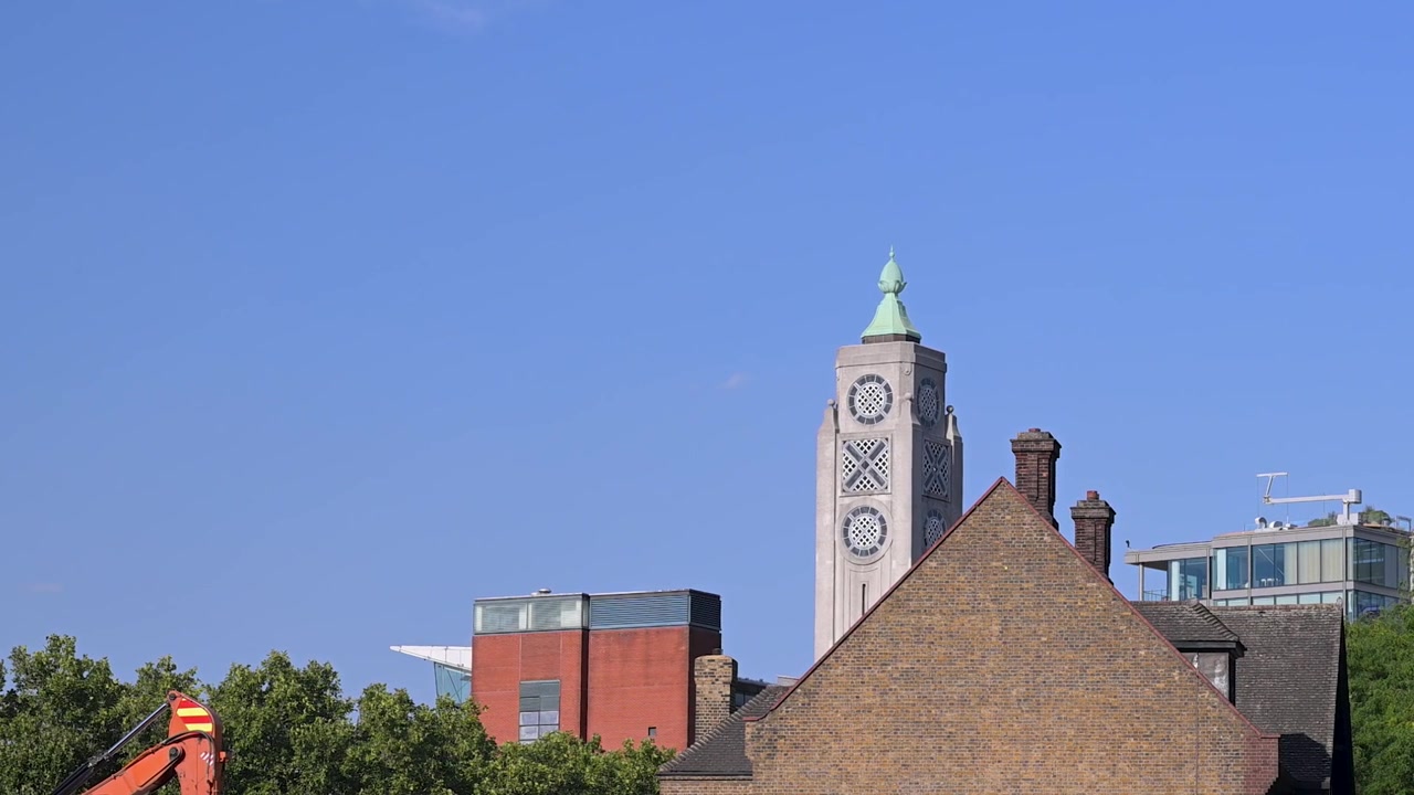 Historiska Oxo Tower klocktorn reser sig över Londons blandade hustak under en klarblå daghimmel.