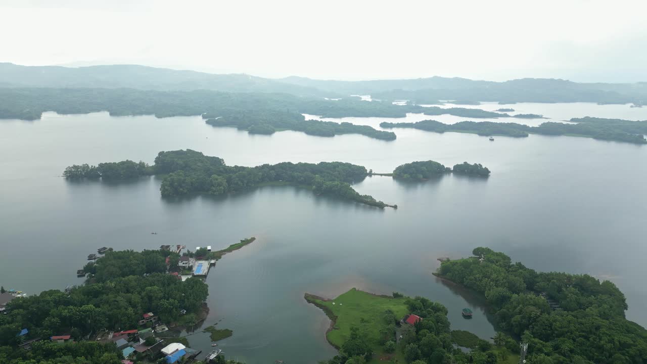 A distant bird’s-eye drone shot swiftly shifts to a top-down view, revealing a vast lake surrounded by trees—capturing expansive natural beauty in Laguna