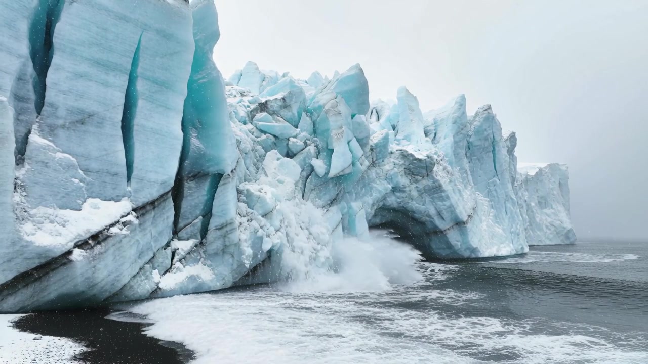 Onda impetuosa che colpisce una scogliera blu bagnata dalla marea in una grotta marina su sabbia nera, causando crolli e spruzzi.