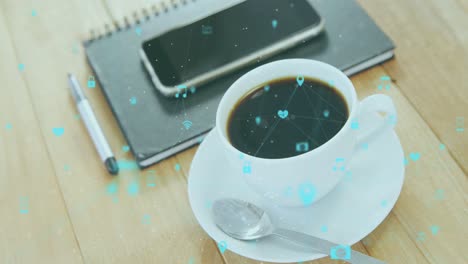 animation of network of digital icons against smartphone, diary and coffee cup on wooden table