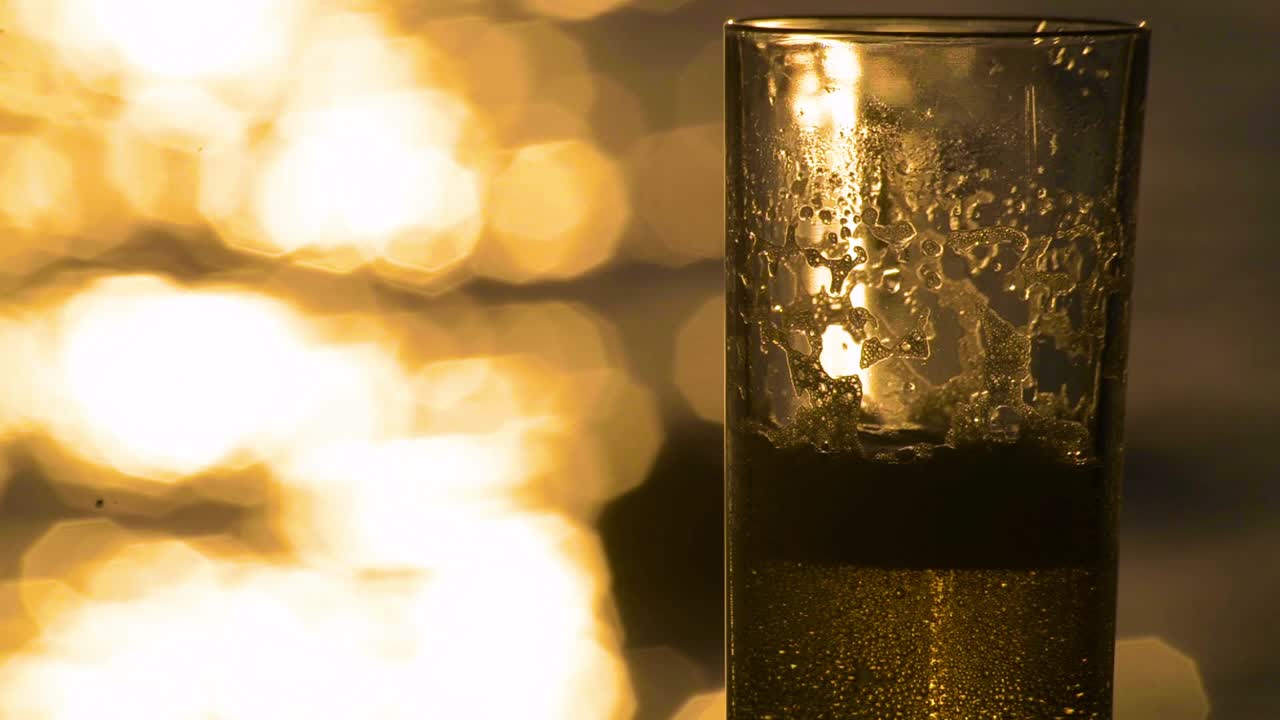 Birra lager chiara ambrata versata in un bicchiere con il mare e il tramonto sullo sfondo.