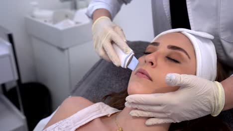 crop beautician doing ultrasound face cleaning for woman in clinic