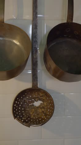 vintage copper kitchen utensils hanging on a tiled wall