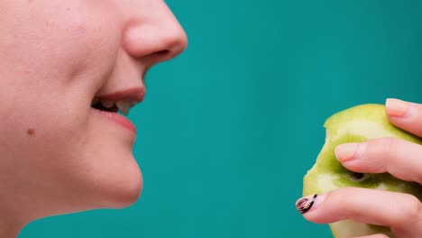 healthy eating and healthy teeth or diet, young woman bites a fresh apple on a green screen close-up