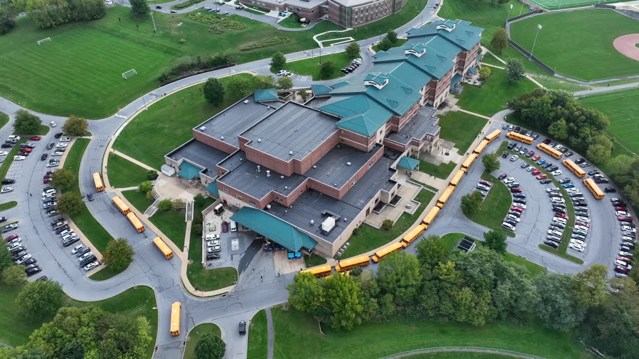 gran escuela secundaria estadounidense con líneas de autobuses escolares amarillos esperando recoger a los estudiantes de la escuela y dejar en las casas