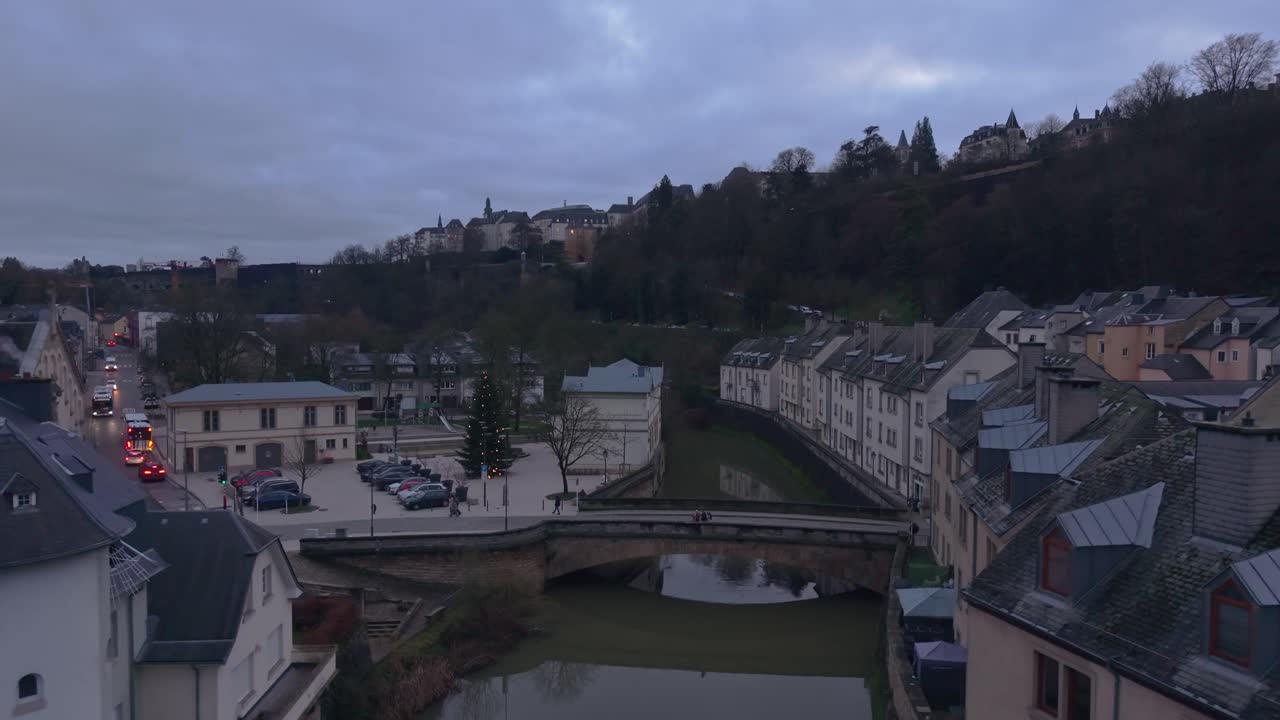 Droneoptagelser af en stenbro over Alzette-floden i Luxembourg, der løfter sig for at afsløre huse langs floden og det fulde panoramiske bybillede over dalen.