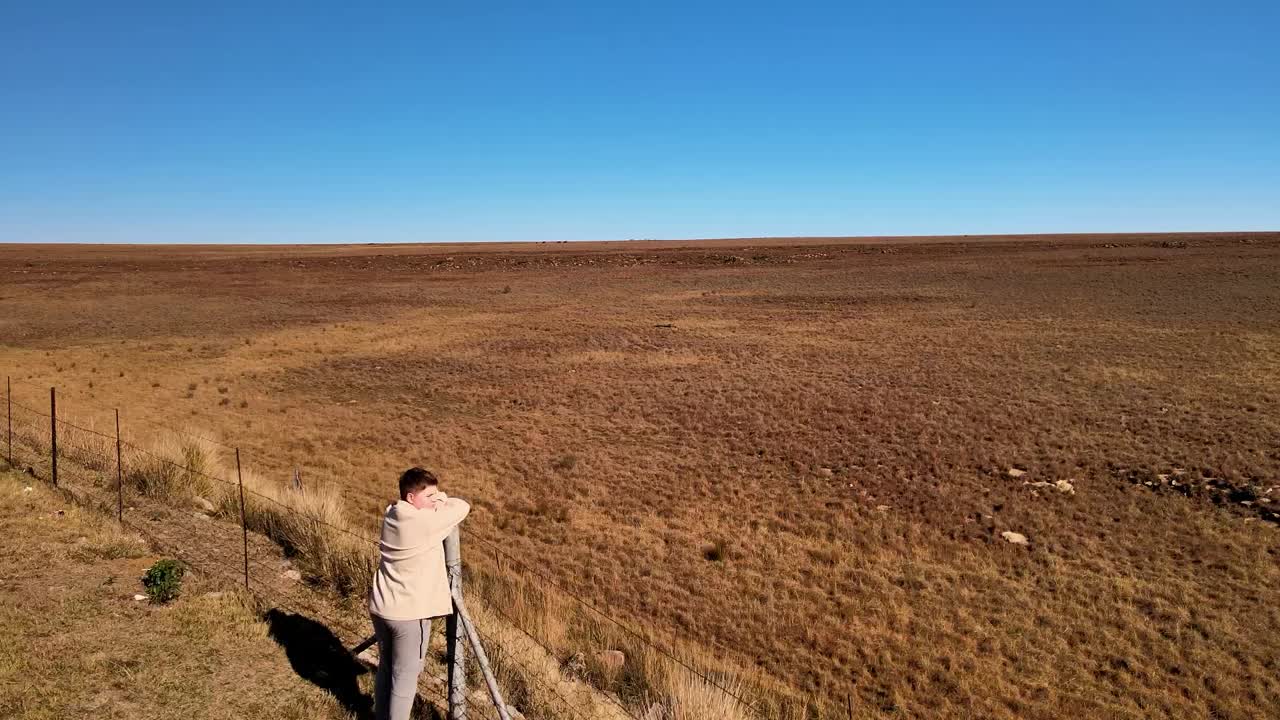 niño caucásico descansando en un poste de la valla, mirando hacia las vastas praderas abiertas en completa libertad