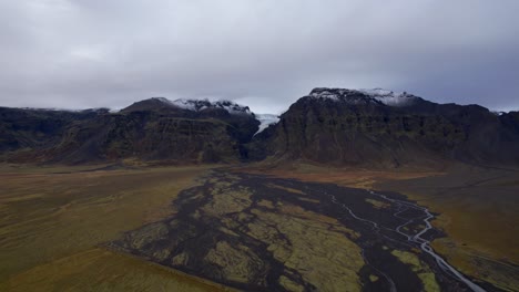 Icelandic-mountains-with-melting-glacier-creating-a-river---Aerial-sideway-flight