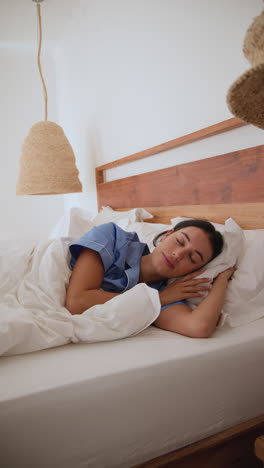 Vertical video: Woman peacefully sleeping in cozy bed with soft white sheets at home