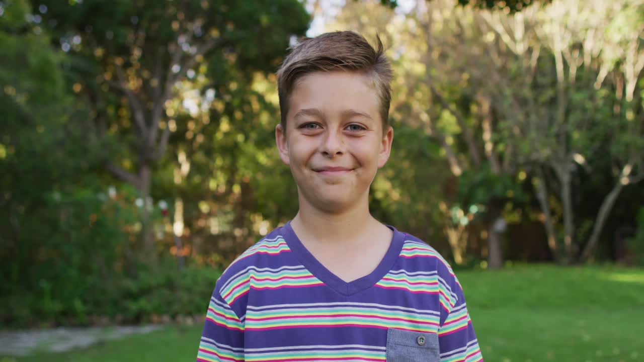 retrato de un niño caucásico feliz de pie en el jardín sonriendo a la cámara