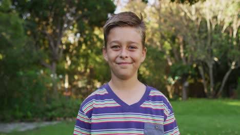 retrato de un niño caucásico feliz de pie en el jardín sonriendo a la cámara