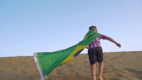 niño con bandera brasileña corriendo en la arena