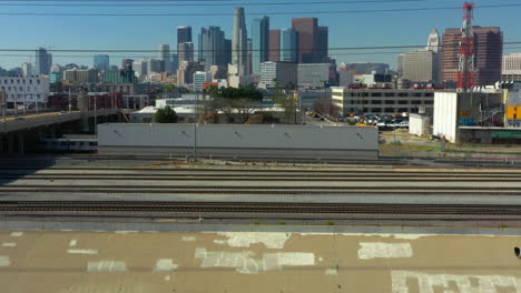 Flying-quickly-over-train-tracks-and-the-LA-river-to-reveal-the-Downtown-Los-Angeles-Skyline-on-a-clear-blue-day,-Drone,-California-USA