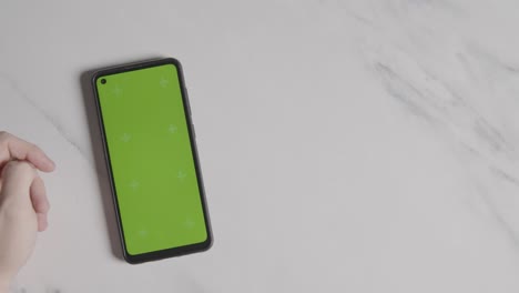 Overhead-Shot-Of-Person-Using-Green-Screen-Mobile-Phone-On-Marble-Surface