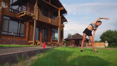 a slim and beautiful woman in sports clothes with an open press is preparing to start training on the lawn near her house performing slopes flexing back muscles