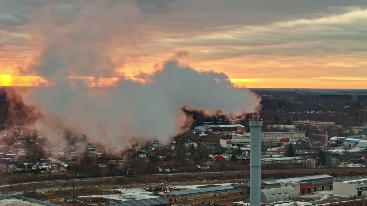 Aerea: ciminiera di un impianto con fumo e un tramonto dal cielo infuocato, ripresa con drone in orbita.