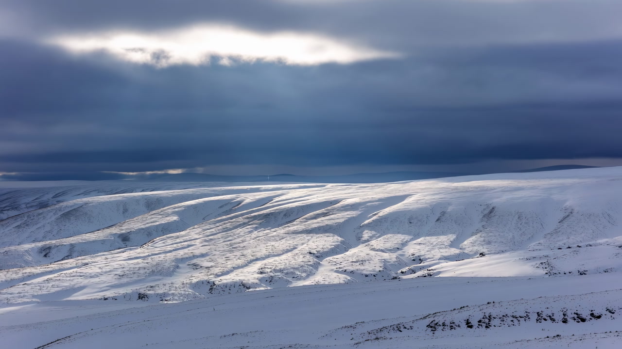 Snowy Mountain Plateau Under Stormy Sky. Pale Light Breaks Through Dense Clouds, Sweeping Across Windsculpted