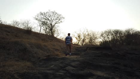 el hombre camina por un sendero natural al aire libre durante la puesta de sol en un bosque y un terreno montañoso