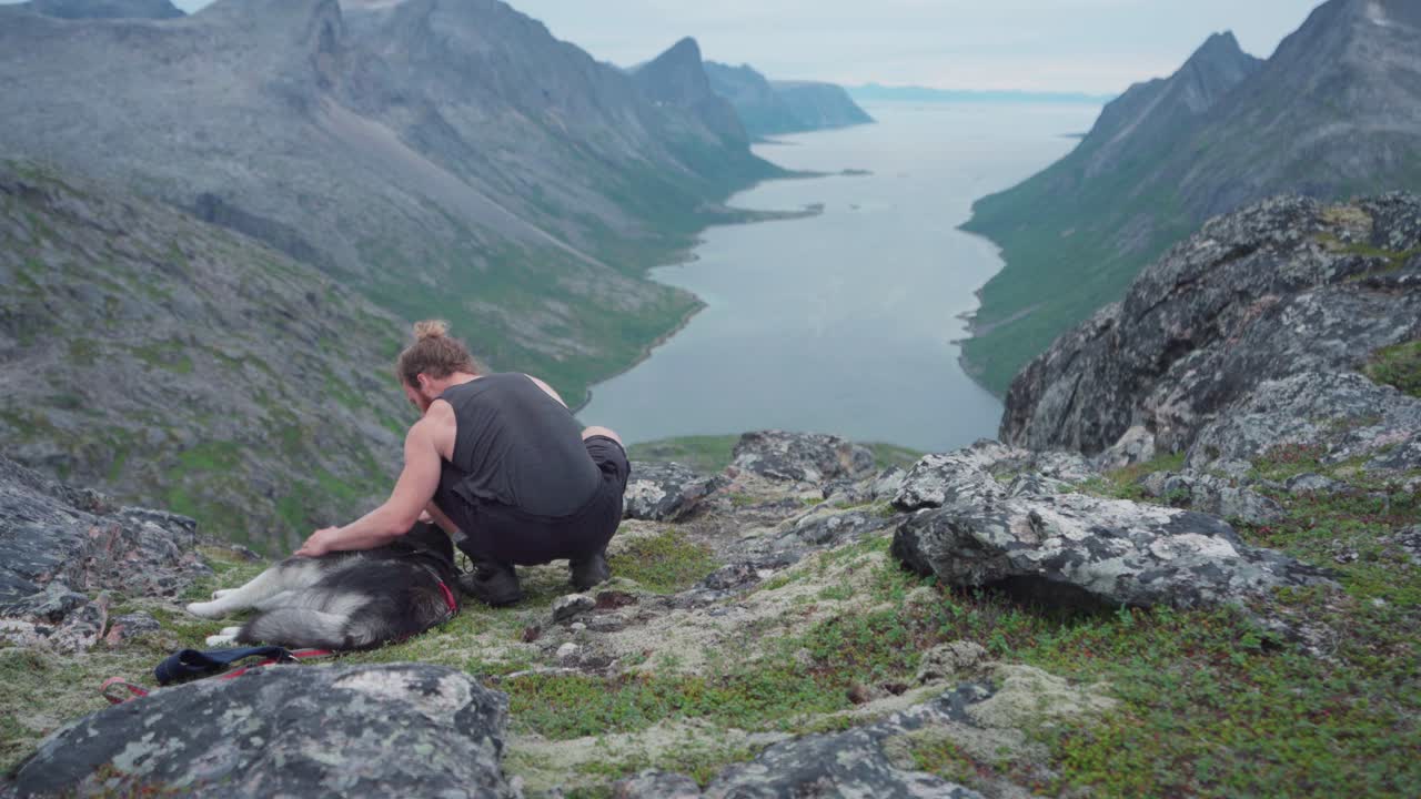 un excursionista caucásico acariciando a su perro mientras descansa en una montaña rocosa en el parque nacional anderdalen en senja, noruega